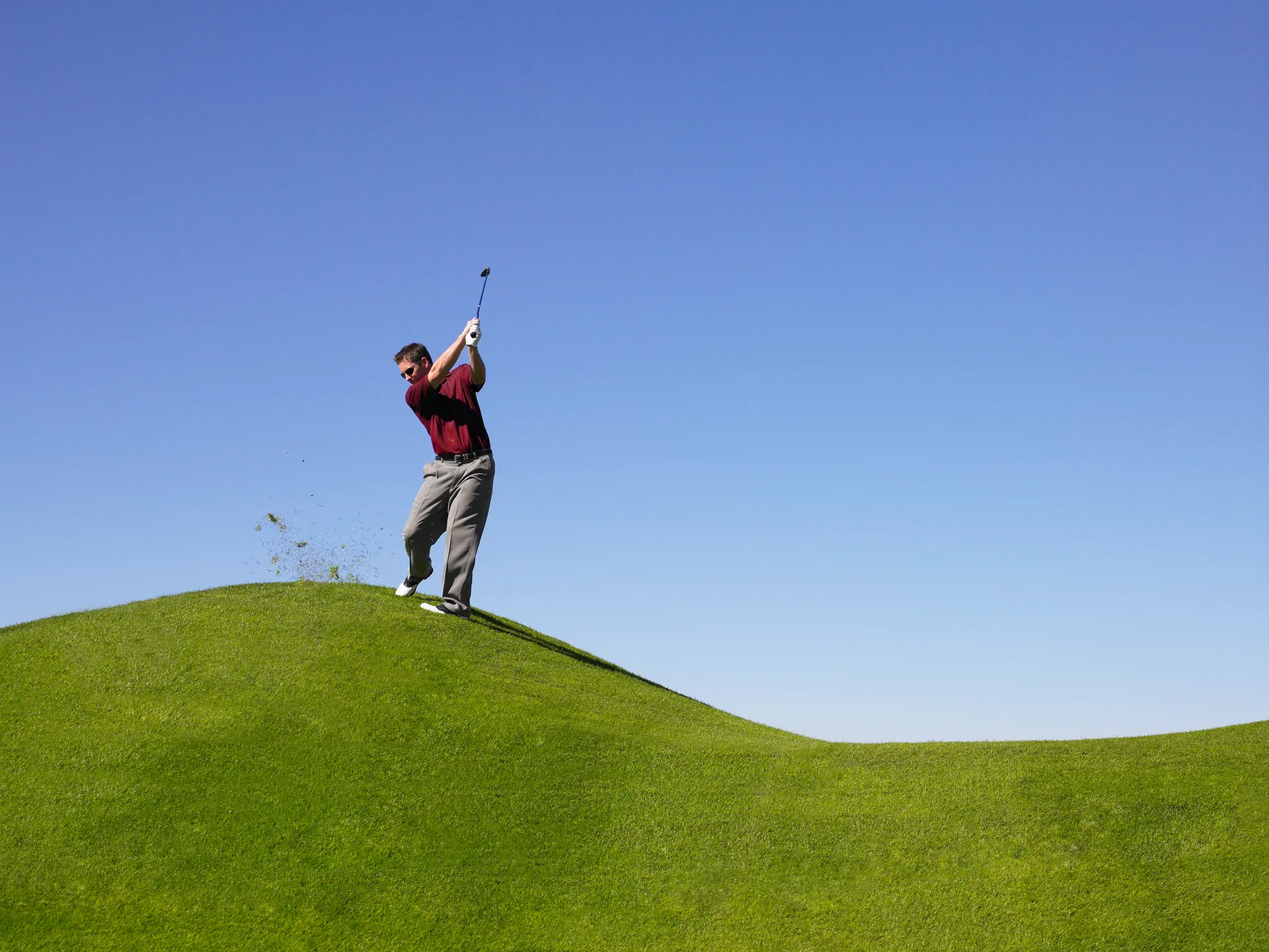 Male golfer hitting from a downhill lie
