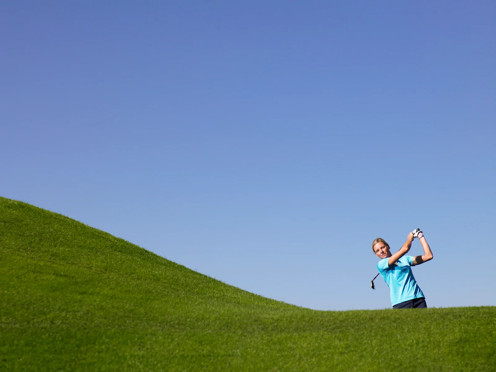 Golfer hitting the ball off a hill above her feet