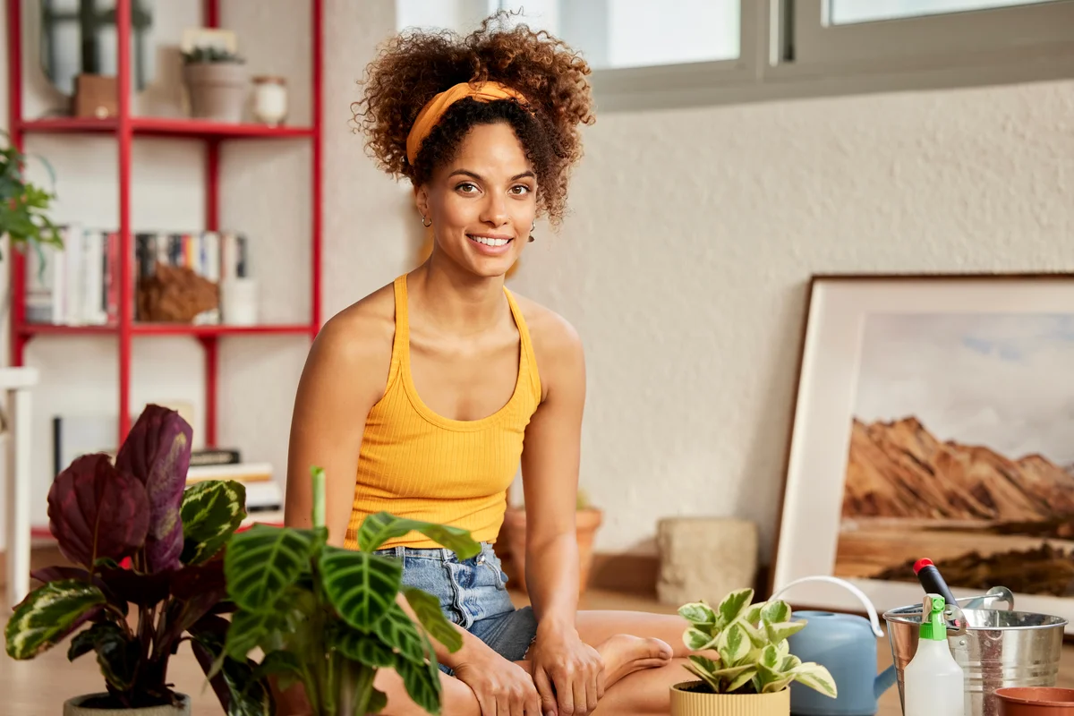 Woman sitting on the floor surrounded by potted plants and pictures